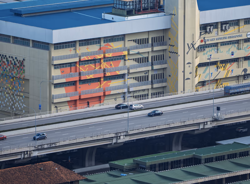 阳光洒在建筑立面与鲜艳壁画上，楼下是公路车流